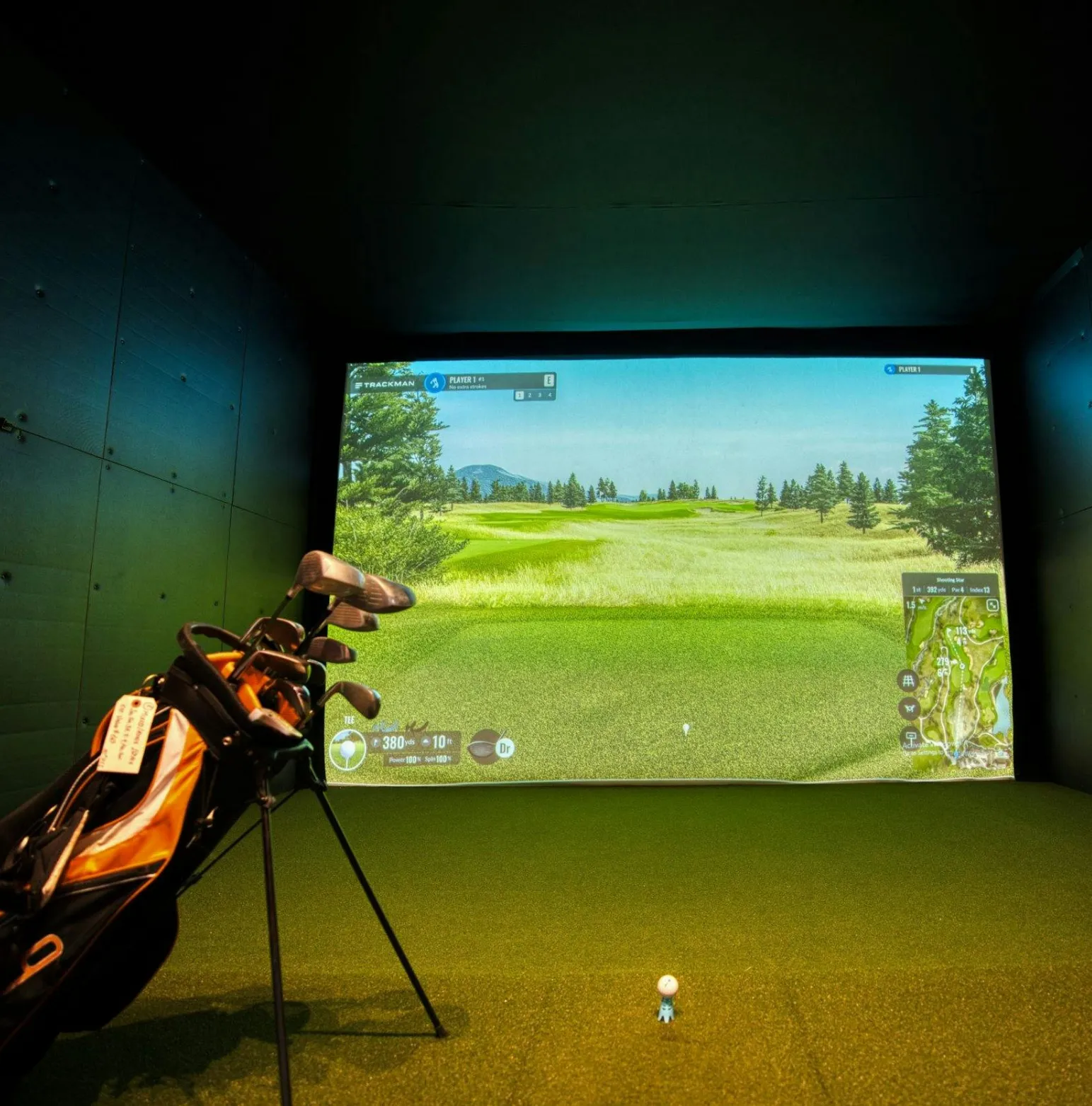 golf-3 Golf clubs and ball in front of a screen showing a golf course in an indoor golf simulator.