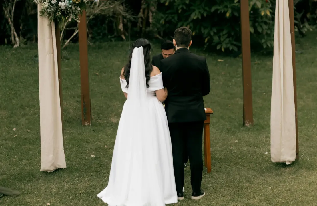 A bride and groom stand together outdoors at an altar, facing away, during their wedding ceremony.